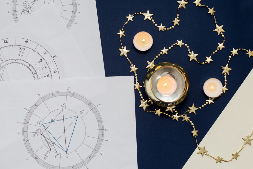 写真：複数枚のホロスコープチャートと、火の灯ったキャンドル、星の形が連なった金のチェーン